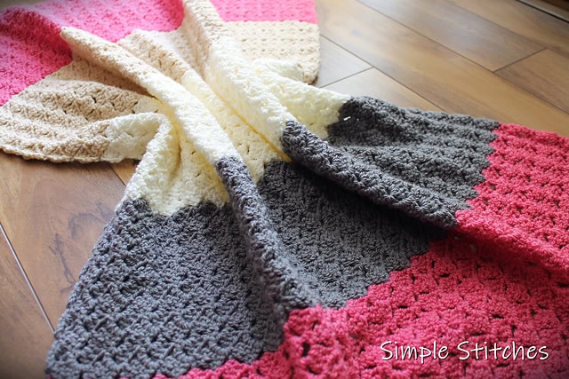 A crochet throw, called the Dallas Blanket, laid out on the floor. The blanket is pink, gray, and cream colors. 