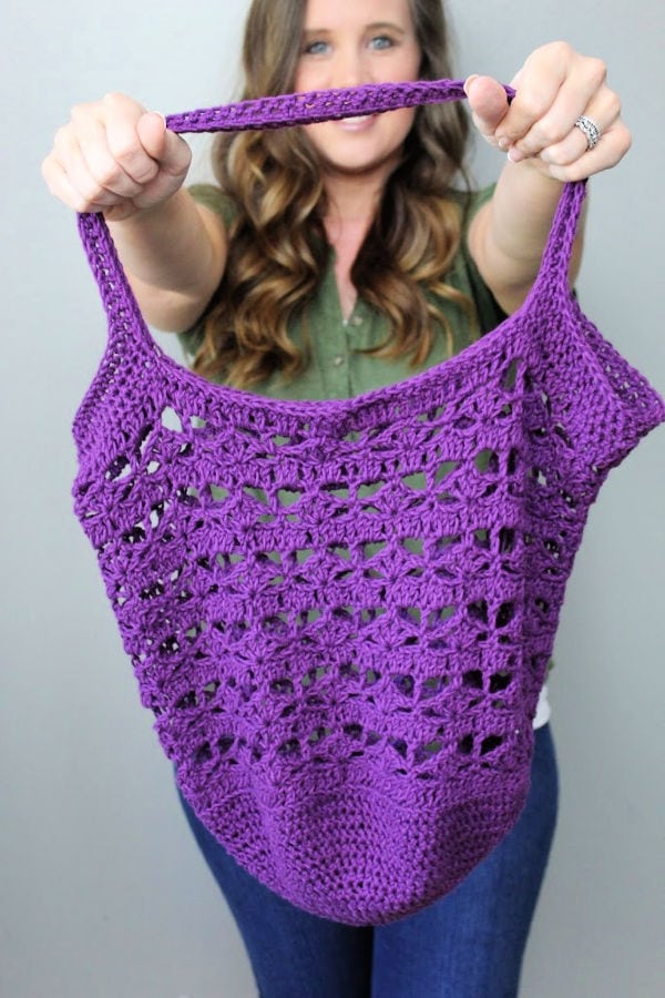 Woman holding up the Calla Lily Market Bag, made in a rich purple color. 