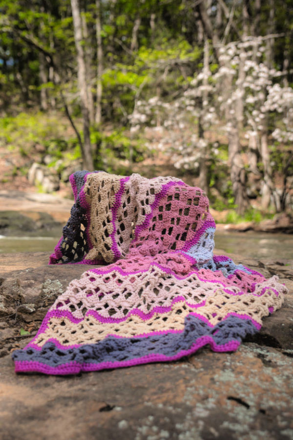 Multicolored throw blanket thrown over a rock with a beautiful stream in the background. 