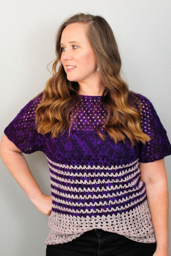 Woman wearing crochet top called the Leilani Raglan Tee. The women's crochet top is  light and dark purple with stripes. 