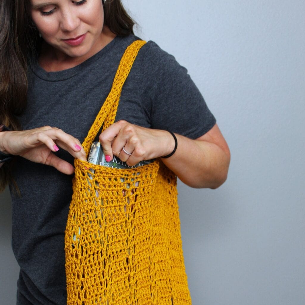 Woman pulling a book out of a crocheted bag, called the Sabre Bag. 