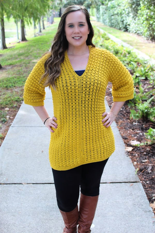 Woman wearing yellow crochet tunic with black leggings and brown boots. 