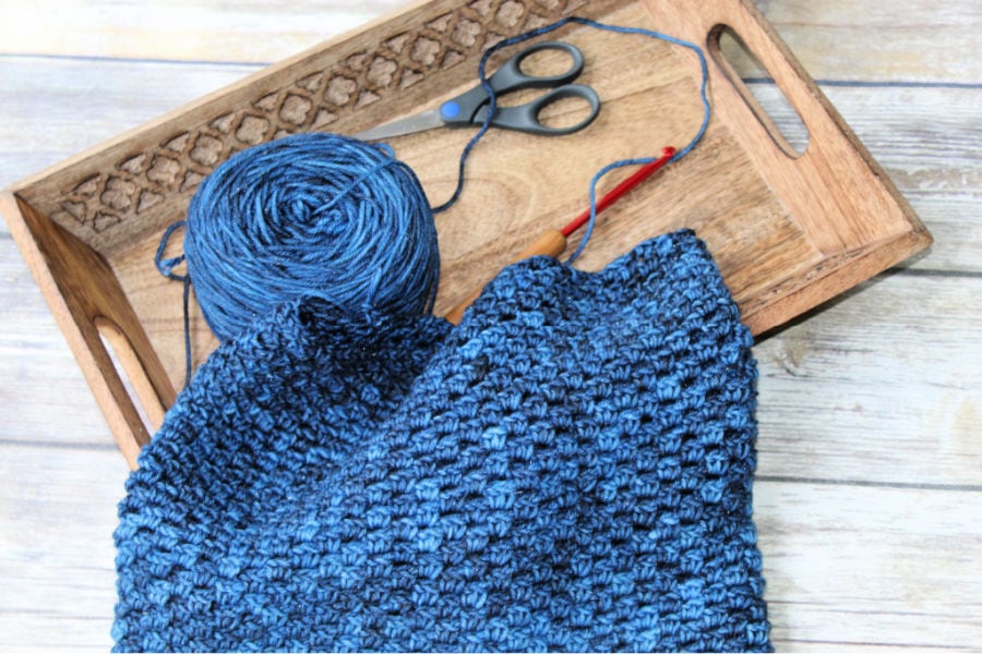 A photo of a Georgia crochet cowl being made with the yarn, crochet hook, and scissors lying in a tray right next to it.