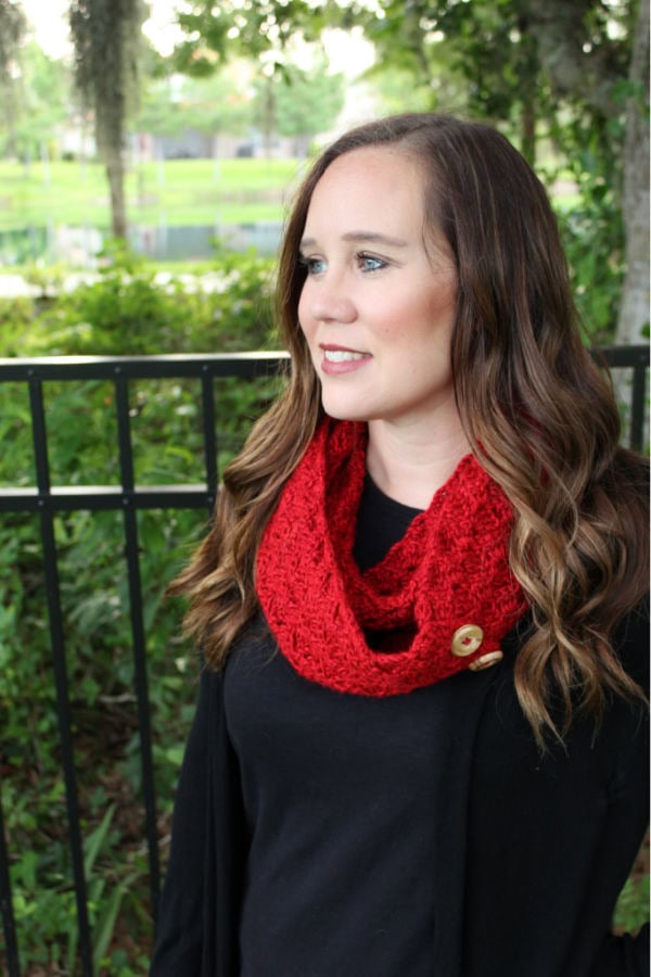 Woman wearing a red crochet infinity scarf with buttons, called the Dallas Scarf.