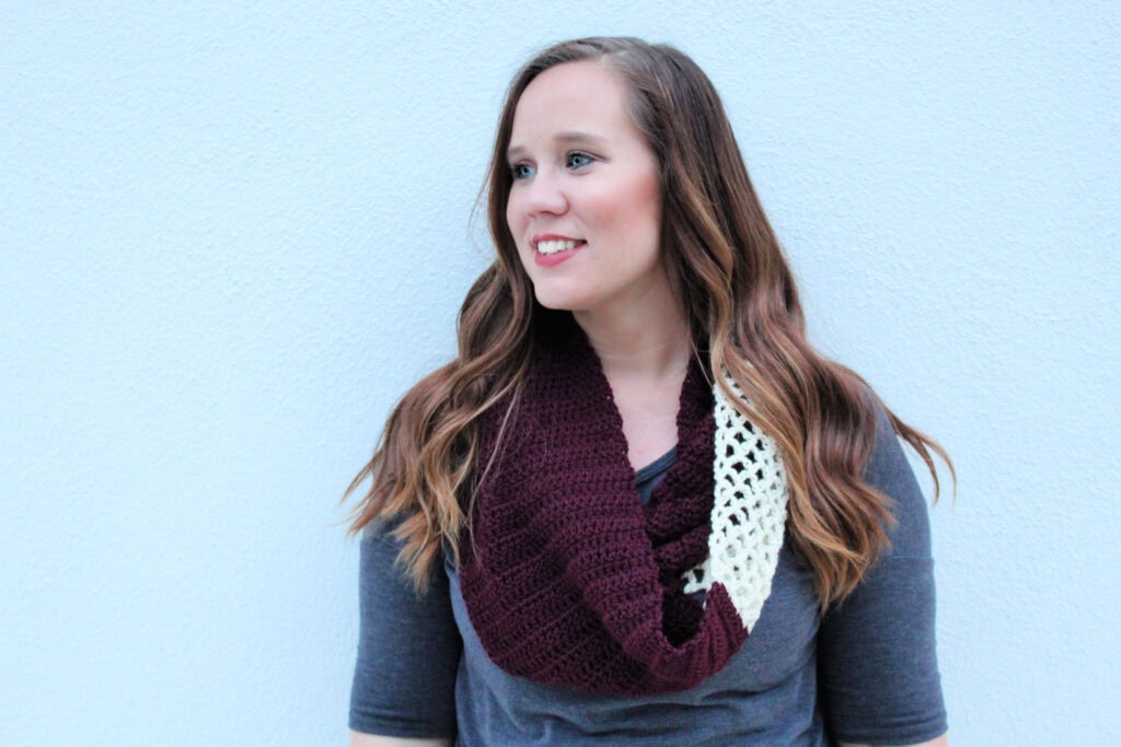 Woman wearing a maroon and cream colored crochet infinity scarf, called the Magnolia Scarf.