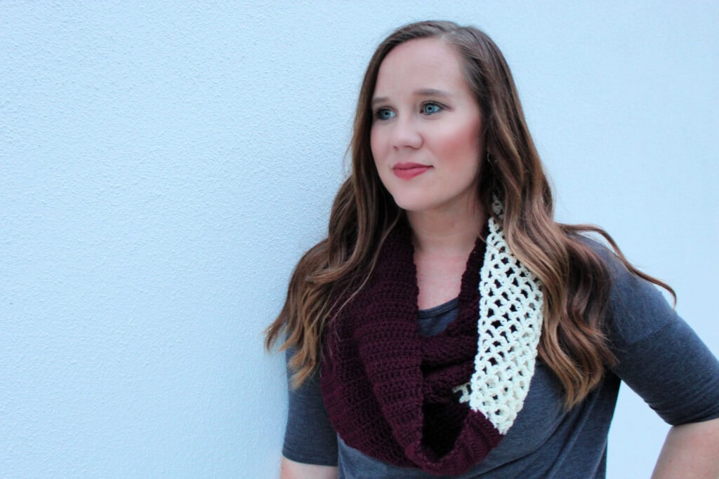 Woman wearing a maroon and cream colored crochet infinity scarf, called the Magnolia Scarf.