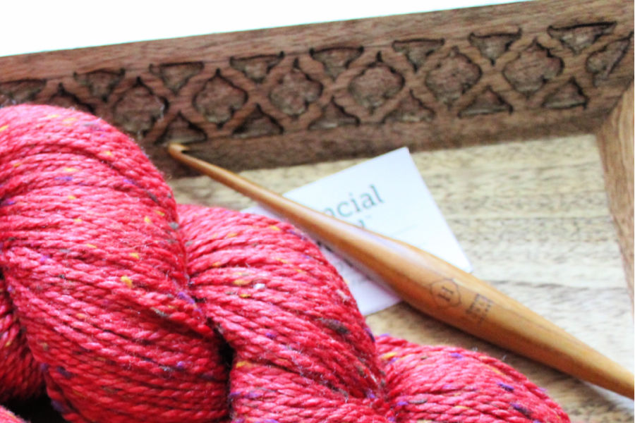 Close up of Furls Streamline crochet hook, lying next to a hank of red yarn. 