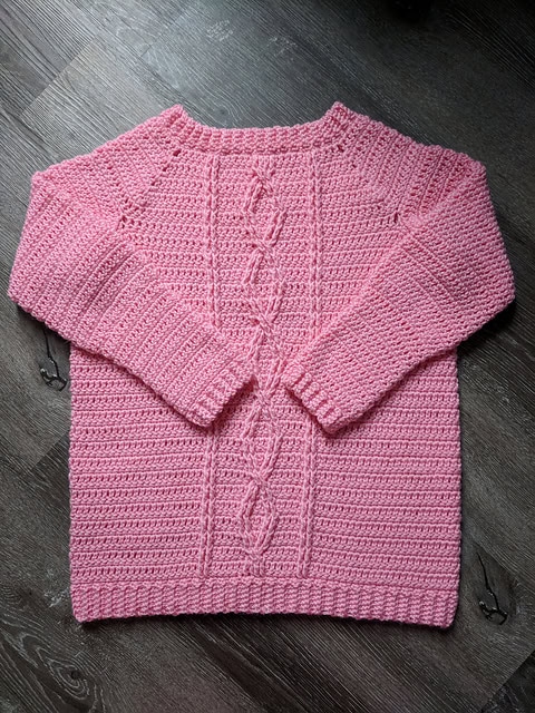 Flat lay of a crochet sweater with cables, called the Crossroads Sweater. 