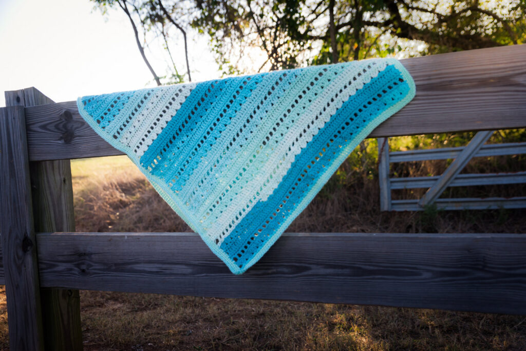 Blue crochet baby blanket laid over a wooden fence. 