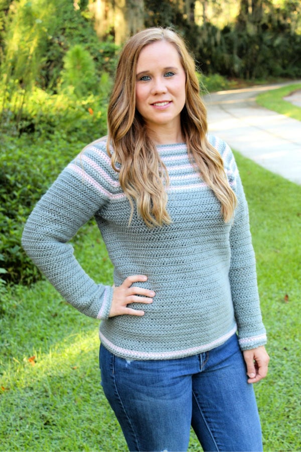 Woman wearing a gray and pink crochet raglan sweater, called the Remi Raglan. 