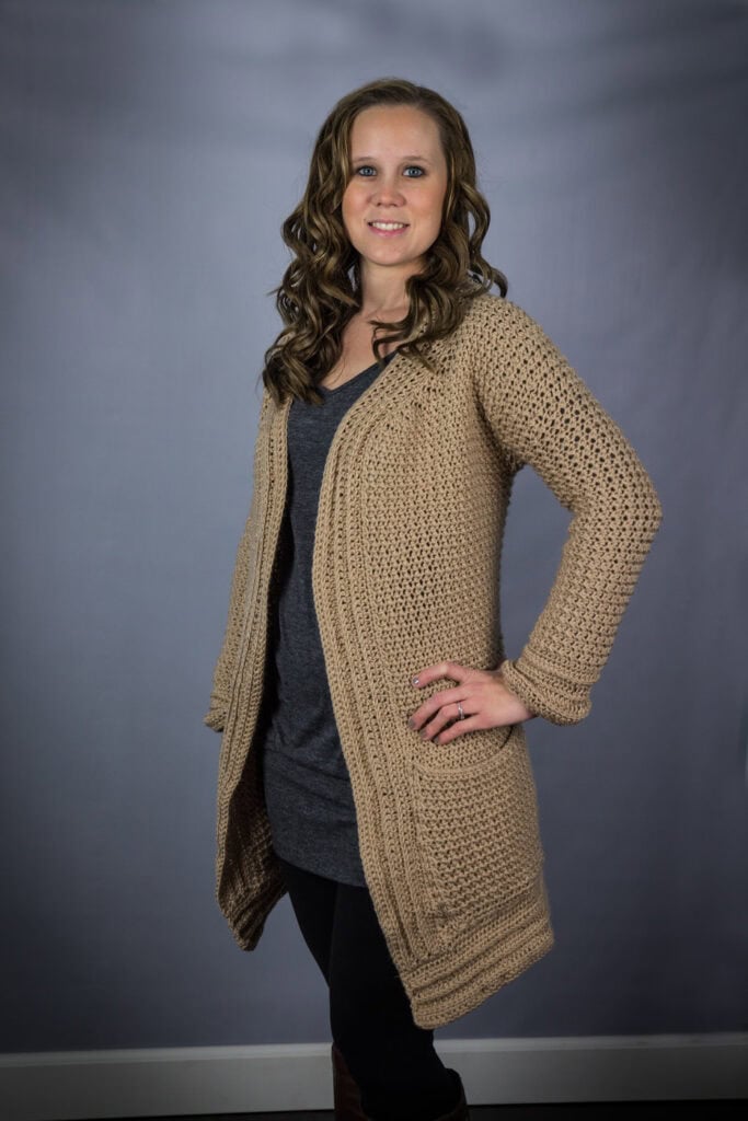 Woman wearing a tan colored crochet cardigan, called the Kristen Cardigan. 