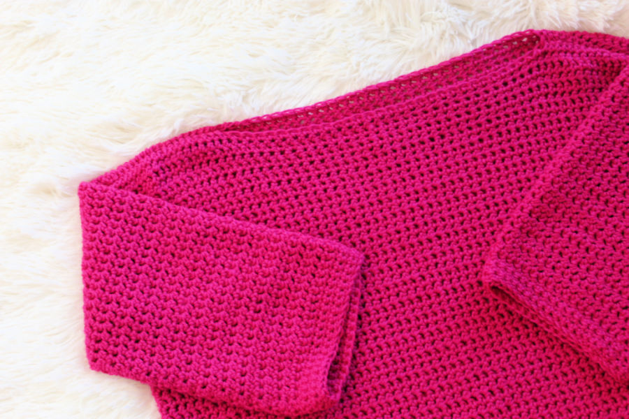 Flat lay photo of a pink crochet sweater, called the Springtime Sweater. 
