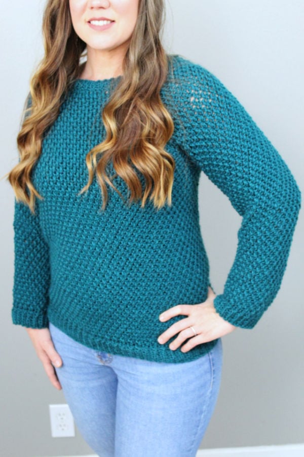 Close up of woman wearing a green crochet sweater, called the Savannah Sweater. 