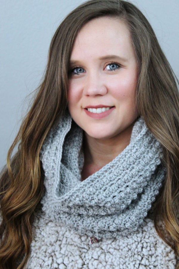 Woman wearing a gray hooded cowl around her neck to demonstrate the ways it can be worn. 