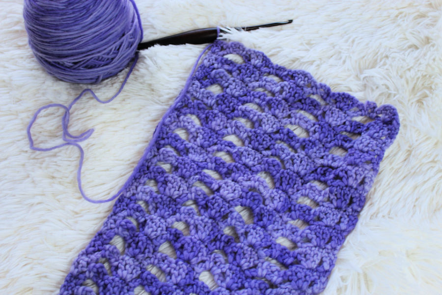Flat lay of light purple yarn and furls crochet hook and partial crochet scarf. 