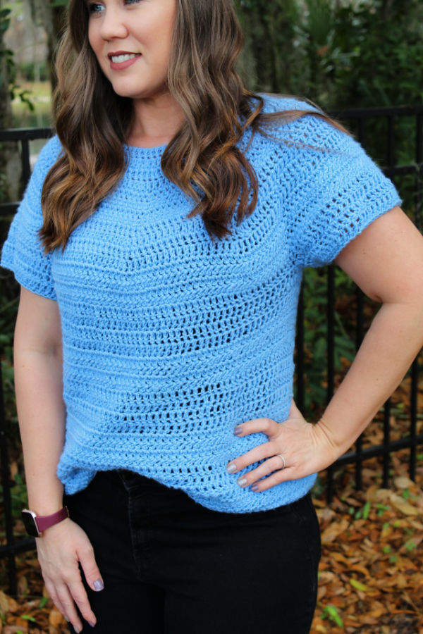 Woman wearing a light blue crochet top, called the Larkin Tee. 