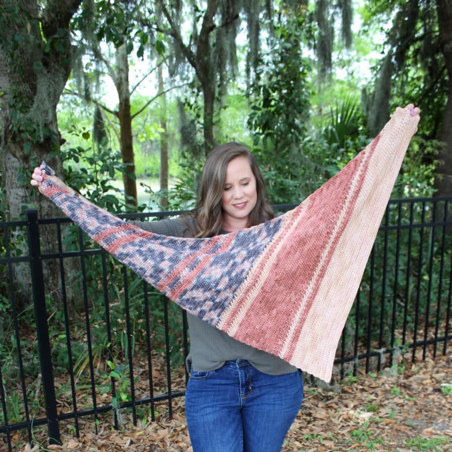 Woman holding up an asymmetrical crochet shawl, called the Amara Shawl. 