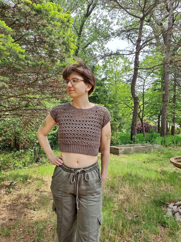 Woman wearing a taupe colored crochet crop top, called the Tuesday Top. 