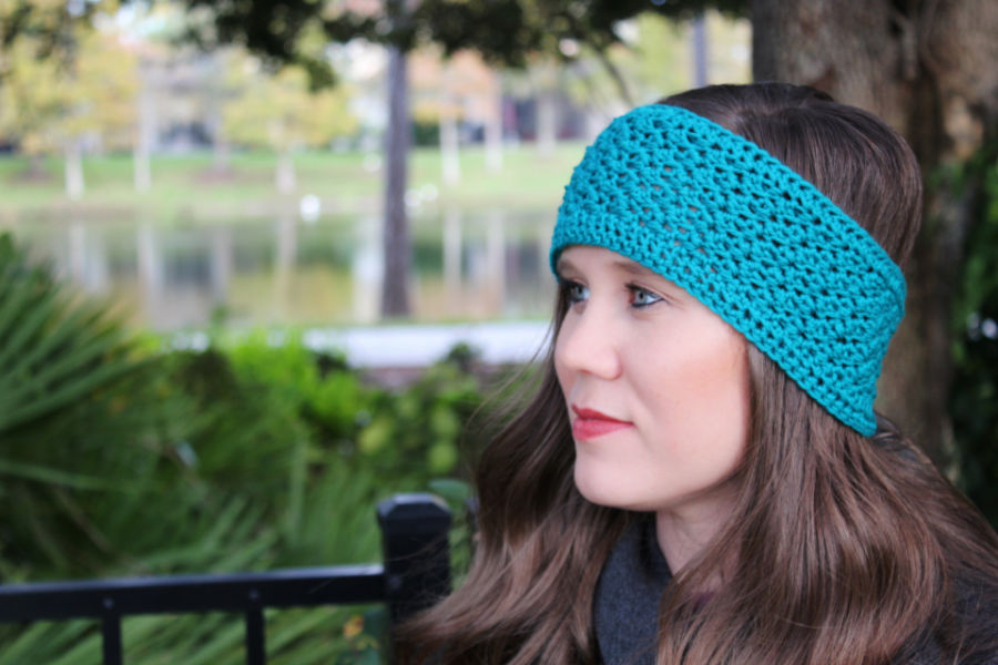 Close up photo of woman wearing a teal crochet earwarmer, called the Boston Earwarmer. 