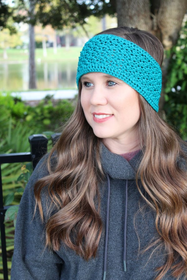 Woman wearing a teal green crochet earwarmer, called the Boston Earwarmer. 