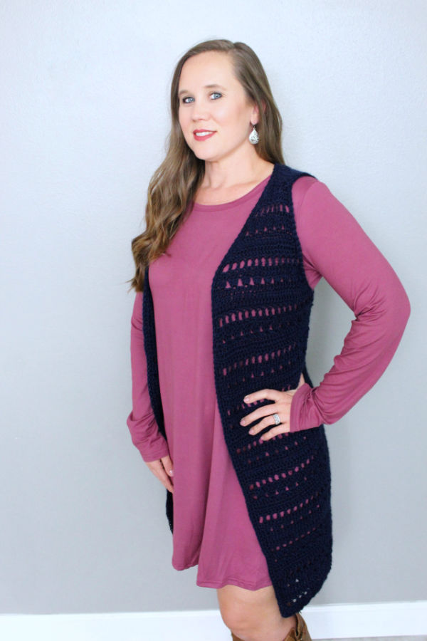Woman in a pink dress wearing a navy blue crochet vest layered over it. 