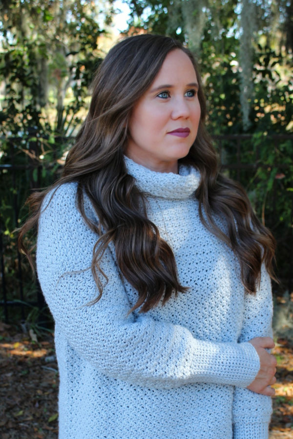 Close up of woman wearing a light gray, oversized crochet sweater, called the Camellia Sweater. 