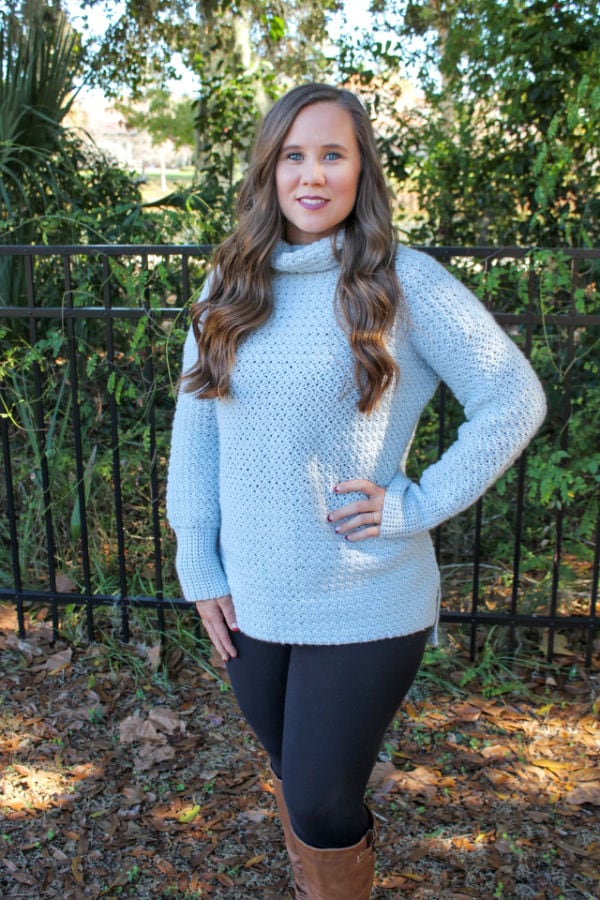 Woman wearing a light gray, oversized crochet sweater, called the Camellia Sweater. 