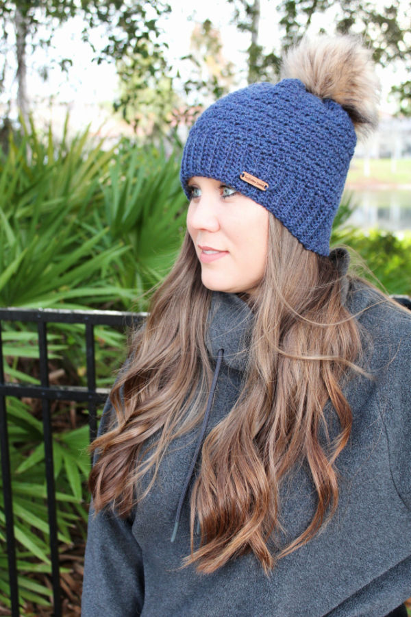 Woman wearing a dark blue crochet hat, called the Camellia Hat. 