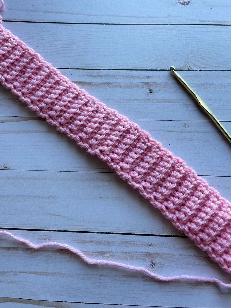 Close up photo of crochet ribbing in pink yarn with a gold crochet hook beside it. 