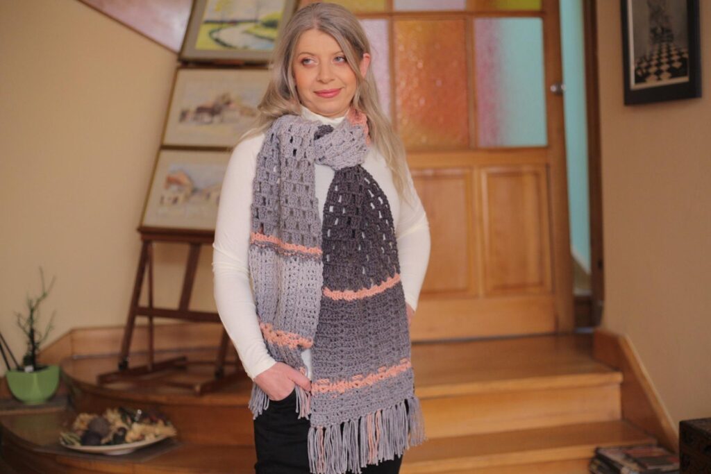 Woman wearing a pink and gray oversized crochet scarf. 