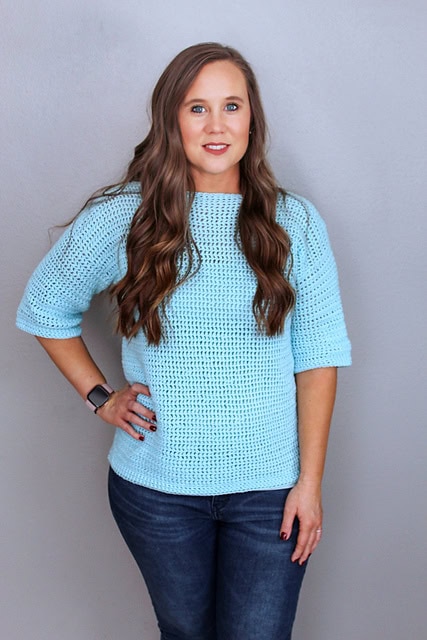 Woman wearing a light blue crochet sweater, called the springtime sweater. 