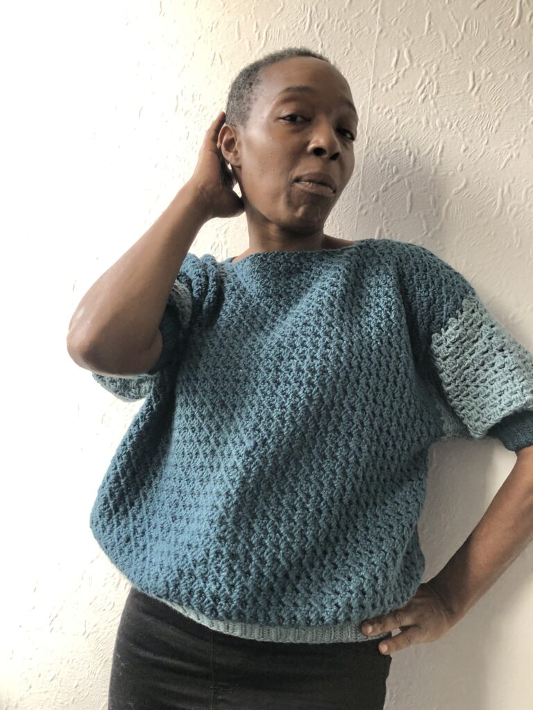 Woman wearing a blue crochet sweater, called the Nain Sweater. 
