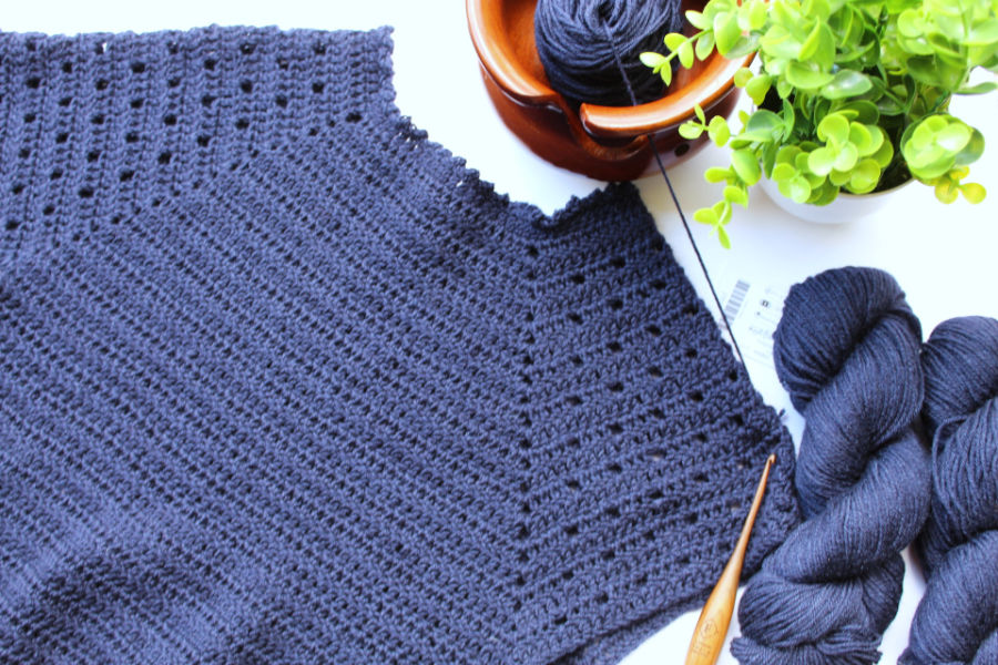Flat lay image of the Plumbago crochet sweater in progress with the yarn and crochet hook lying next to it. 