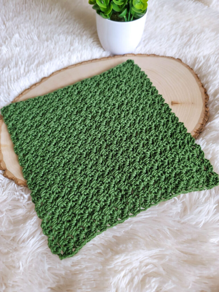 A green crochet washcloth laid out on a piece of wood. 