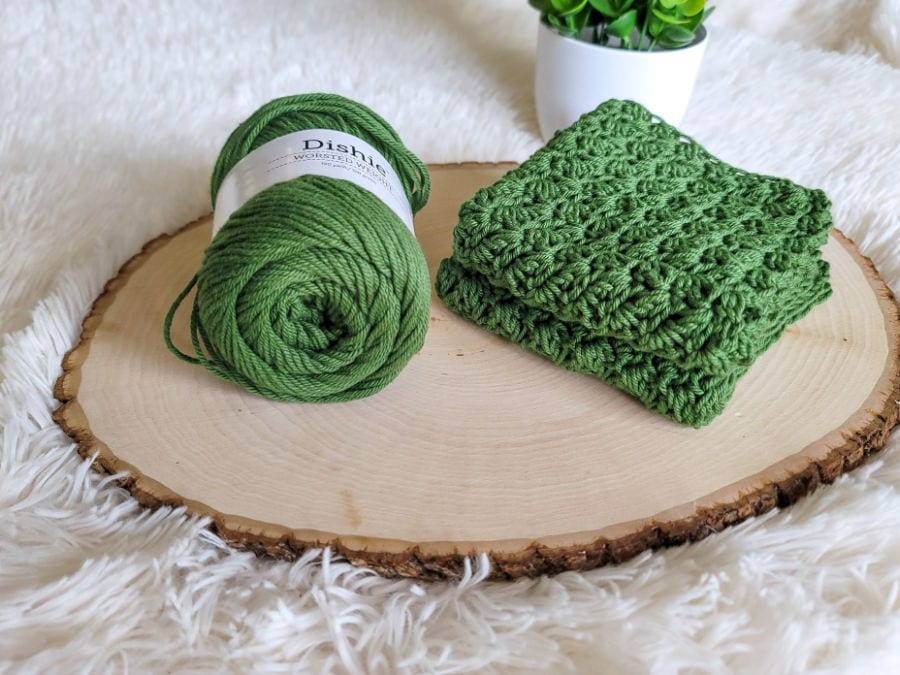 A green crochet washcloth folded and the yarn used to make it right next to it. 