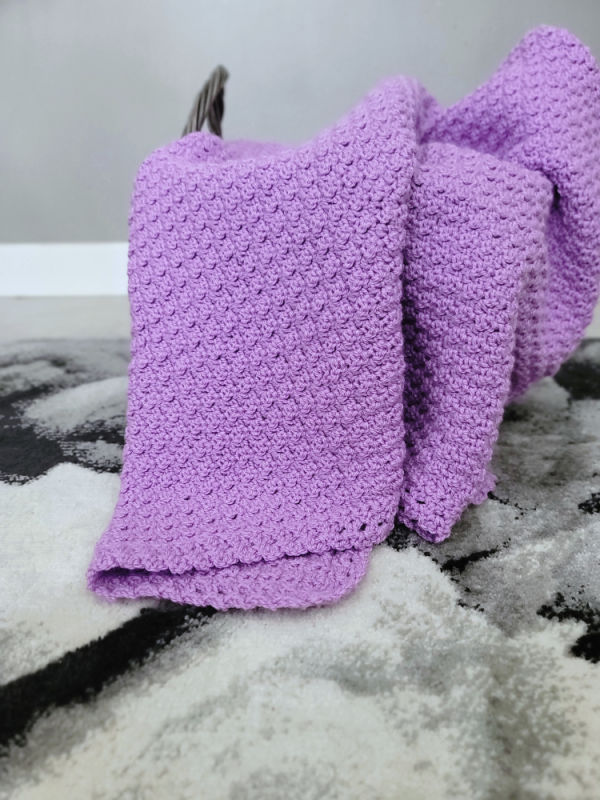 Light purple crochet baby blanket folded into a basket. 