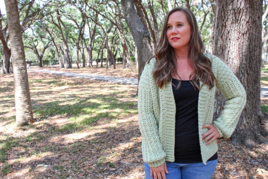 Woman wearing a green crochet cardigan, called the Blossoming Sprigs Cardigan.