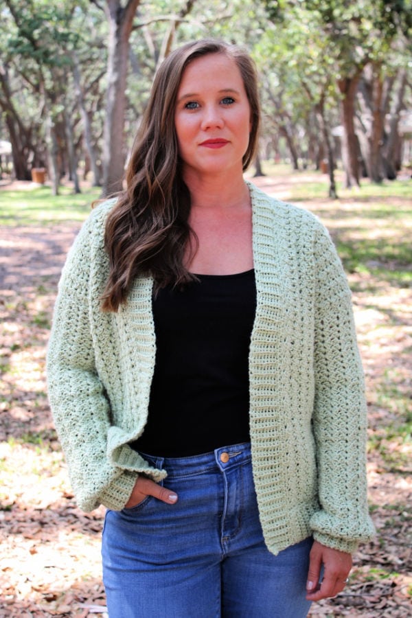 Woman wearing a green crochet cardigan, called the Blossoming Sprigs cardigan.
