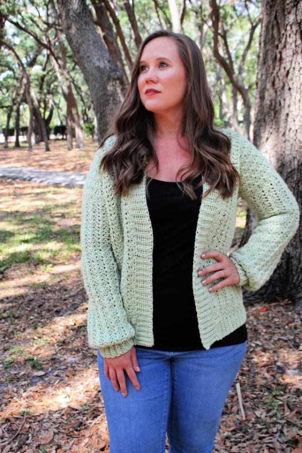 Woman wearing a green crochet cardigan, called the Blossoming Sprigs Cardigan.