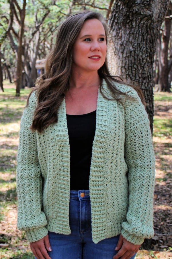 Woman wearing a green crochet cardigan, called the Blossoming Sprigs Cardigan.