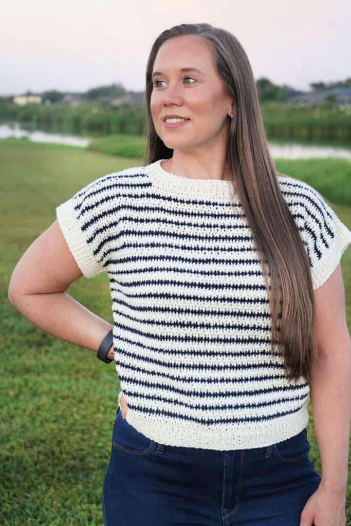 Close up view of woman wearing a short-sleeved sweater with stripes in cream and navy.