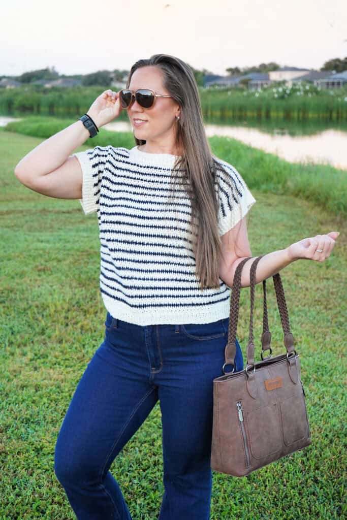Woman wearing a short-sleeved crochet sweater in the color cream with navy stripes throughout.